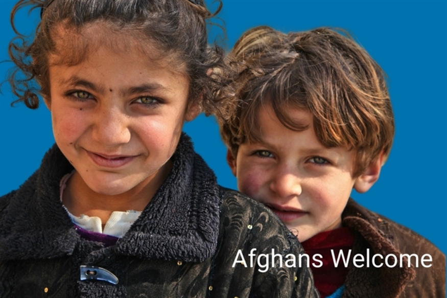 [ai] Two children, a girl and a boy, are smiling. The girl has curly dark hair and wears a black coat, while the boy has light brown hair. A blue background includes the text 'Afghans Welcome'.